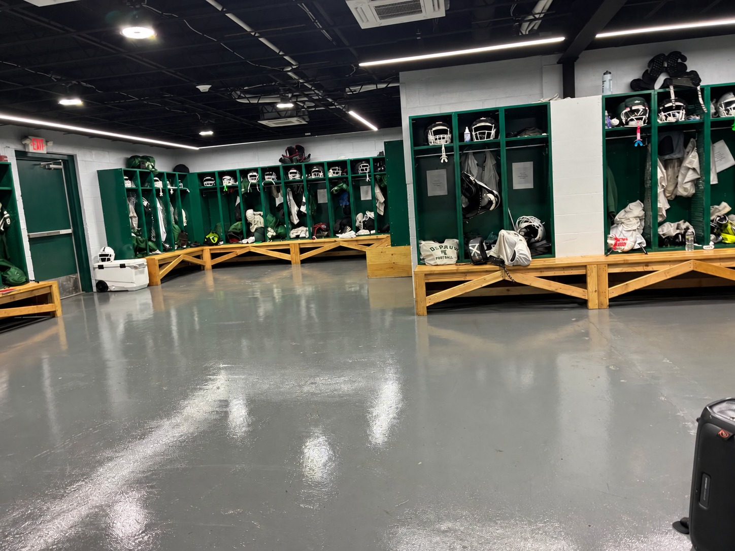 Athletic locker room with green lockers, benches, and gray flooring